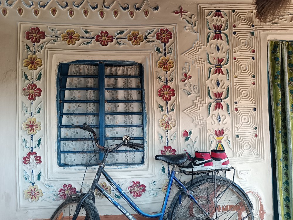 Tharu mud-wall mural in Eastern Nepal with raised clay floral, geometric, bird and animal motifs around a window